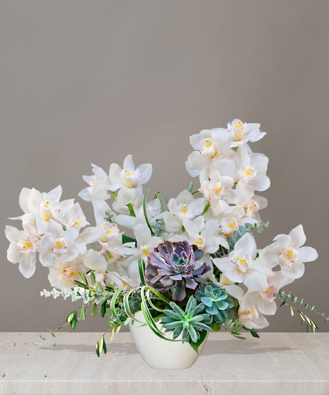 Luxurious Bali floral arrangement with cascading white cymbidium orchids, lush succulents, and greenery in a modern white vase on a marble table.