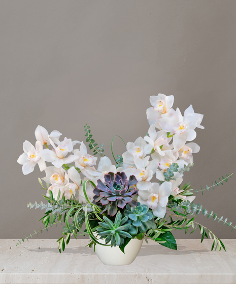 Luxurious Bali floral arrangement with cascading white cymbidium orchids, lush succulents, and greenery in a modern white vase on a marble table.