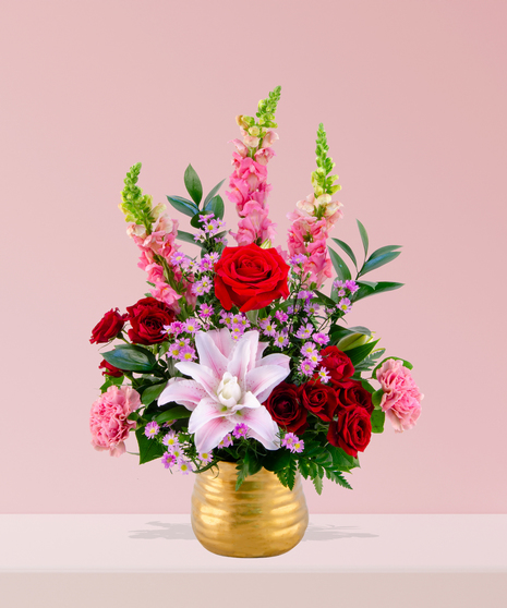 A luxurious arrangement of red roses, pink lilies, snapdragons, carnations, and lavender daisies in a gold vase, handcrafted by Billy Heroman’s Florist in Baton Rouge, LA.