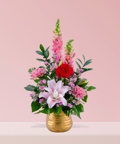 A luxurious arrangement of red roses, pink lilies, snapdragons, carnations, and lavender daisies in a gold vase, handcrafted by Billy Heroman’s Florist in Baton Rouge, LA.