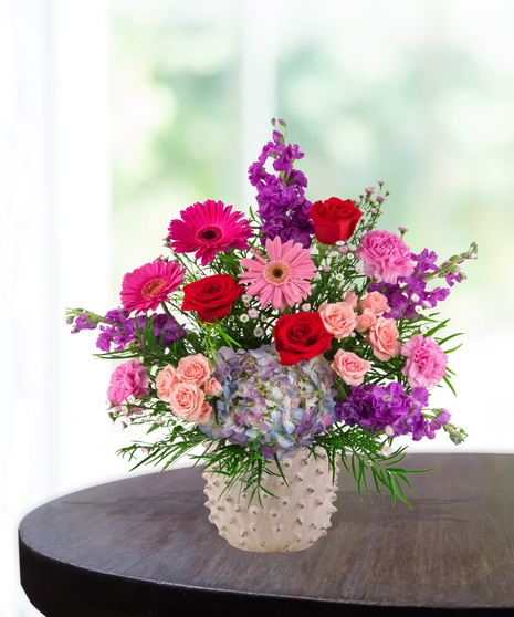 A vibrant flower arrangement featuring red roses, pink gerbera daisies, and more in a lavender vase, exclusively from Billy Heroman’s Florist in Baton Rouge, LA.