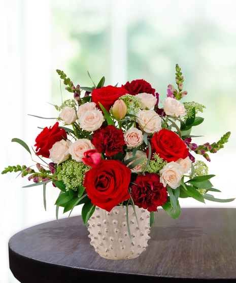 Garnet N' Roses floral arrangement with red roses, fuchsia garden roses, blush spray roses, and burgundy snapdragons in a textured white ceramic vase.