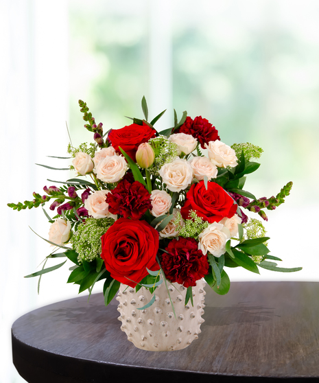 Garnet N' Roses floral arrangement with red roses, fuchsia garden roses, blush spray roses, and burgundy snapdragons in a textured white ceramic vase.