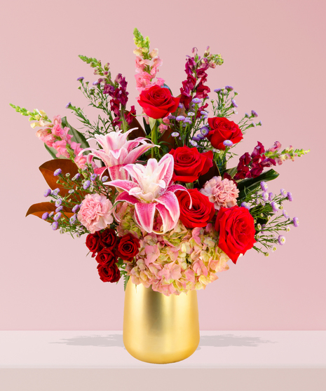 A luxurious Valentine’s Day bouquet featuring red roses, pink stargazer lilies, hydrangeas, and snapdragons in a gold-toned vase by Billy Heroman’s in Baton Rouge.