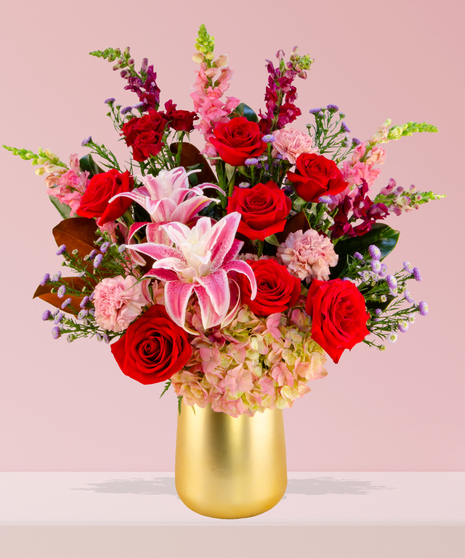 A luxurious Valentine’s Day bouquet featuring red roses, pink stargazer lilies, hydrangeas, and snapdragons in a gold-toned vase by Billy Heroman’s in Baton Rouge.