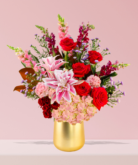 A luxurious Valentine’s Day bouquet featuring red roses, pink stargazer lilies, hydrangeas, and snapdragons in a gold-toned vase by Billy Heroman’s in Baton Rouge.