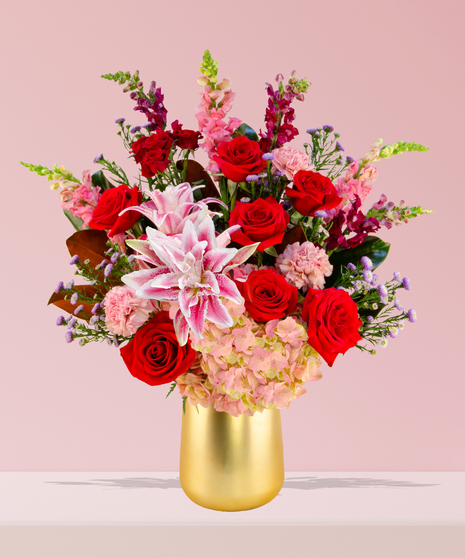 A luxurious Valentine’s Day bouquet featuring red roses, pink stargazer lilies, hydrangeas, and snapdragons in a gold-toned vase by Billy Heroman’s in Baton Rouge.