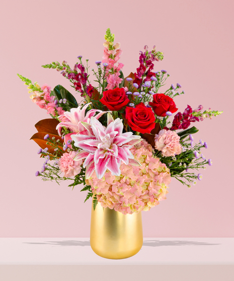 A luxurious Valentine’s Day bouquet featuring red roses, pink stargazer lilies, hydrangeas, and snapdragons in a gold-toned vase by Billy Heroman’s in Baton Rouge.