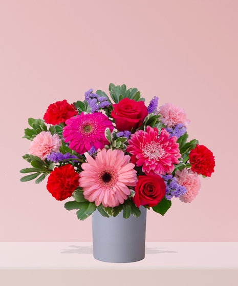 A vibrant Valentine’s Day bouquet with red roses, pink gerbera daisies, carnations, and lavender statice, arranged in a modern gray vase by Billy Heroman’s in Baton Rouge.