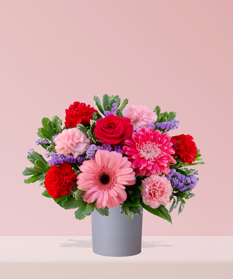 A vibrant Valentine’s Day bouquet with red roses, pink gerbera daisies, carnations, and lavender statice, arranged in a modern gray vase by Billy Heroman’s in Baton Rouge.