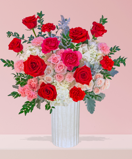 P.S. I Love You Valentine’s Day floral arrangement with red roses, fuchsia garden roses, pink spray roses, and carnations in a white textured vase.