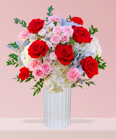 P.S. I Love You Valentine’s Day floral arrangement with red roses, fuchsia garden roses, pink spray roses, and carnations in a white textured vase.