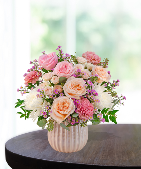 Blush Parlor floral arrangement featuring pink garden roses, spray roses, white chrysanthemums, carnations, and aster in a textured ceramic vase.