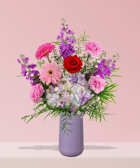 A vibrant flower arrangement featuring red roses, pink gerbera daisies, and more in a lavender vase, exclusively from Billy Heroman’s Florist in Baton Rouge, LA.