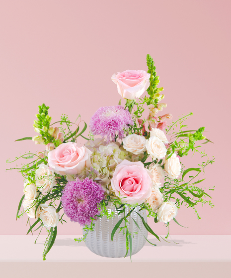 Smitten floral arrangement with peach and pink roses, lavender mums, and snapdragons in a white textured vase.