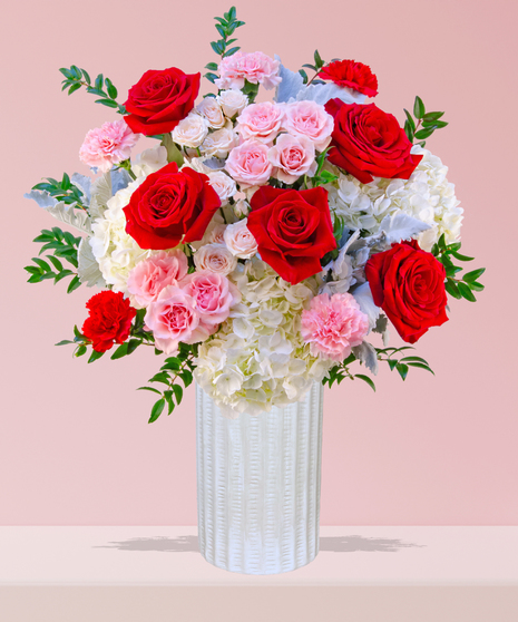 P.S. I Love You Valentine’s Day floral arrangement with red roses, fuchsia garden roses, pink spray roses, and carnations in a white textured vase.