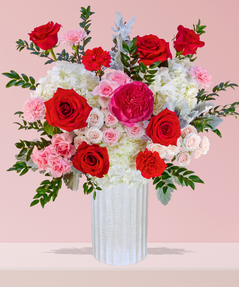 P.S. I Love You Valentine’s Day floral arrangement with red roses, fuchsia garden roses, pink spray roses, and carnations in a white textured vase.