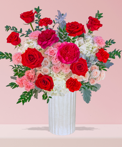 P.S. I Love You Valentine’s Day floral arrangement with red roses, fuchsia garden roses, pink spray roses, and carnations in a white textured vase.