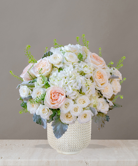 Billy Heroman's Signature Collection white and blush flower arrangement with roses, hydrangeas, and greenery in a textured white vase