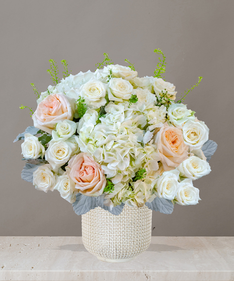 Billy Heroman's Signature Collection white and blush flower arrangement with roses, hydrangeas, and greenery in a textured white vase