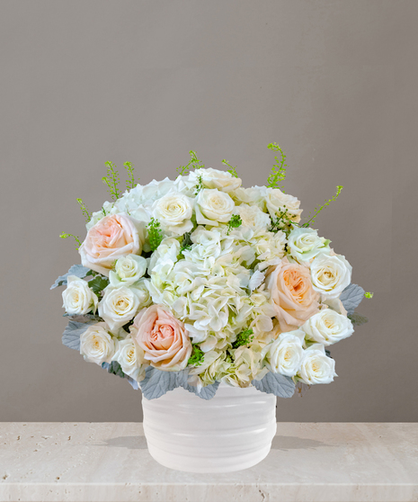 Billy Heroman's Signature Collection white and blush flower arrangement with roses, hydrangeas, and greenery in a textured white vase