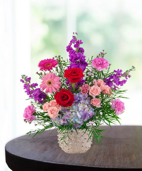 A vibrant flower arrangement featuring red roses, pink gerbera daisies, and more in a lavender vase, exclusively from Billy Heroman’s Florist in Baton Rouge, LA.