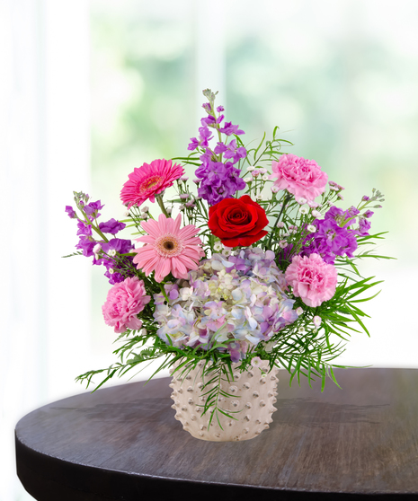 A vibrant flower arrangement featuring red roses, pink gerbera daisies, and more in a lavender vase, exclusively from Billy Heroman’s Florist in Baton Rouge, LA.