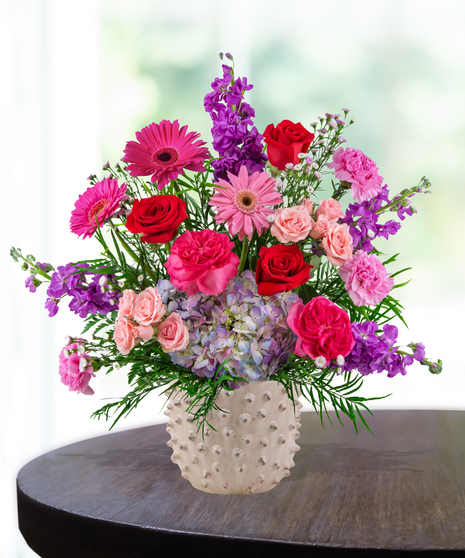 A vibrant flower arrangement featuring red roses, pink gerbera daisies, and more in a lavender vase, exclusively from Billy Heroman’s Florist in Baton Rouge, LA.