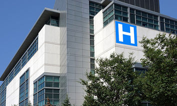 A white multi-story building (hospital) with large windows features a prominent blue 